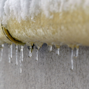 A yellow pipe on a cement wall, covered in ice and ice sickles