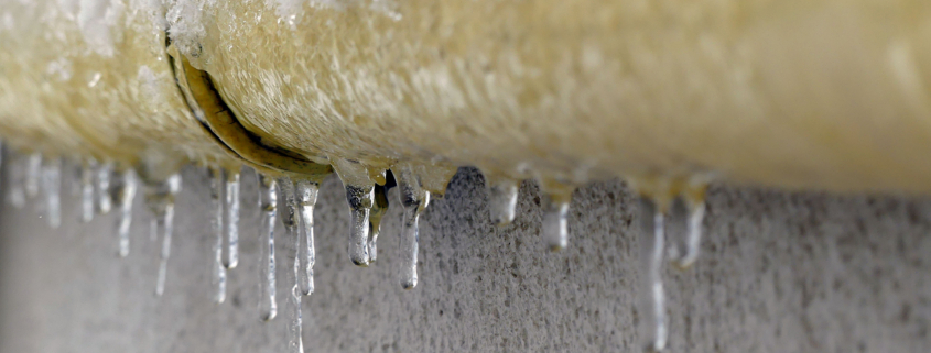 A yellow pipe on a cement wall, covered in ice and ice sickles
