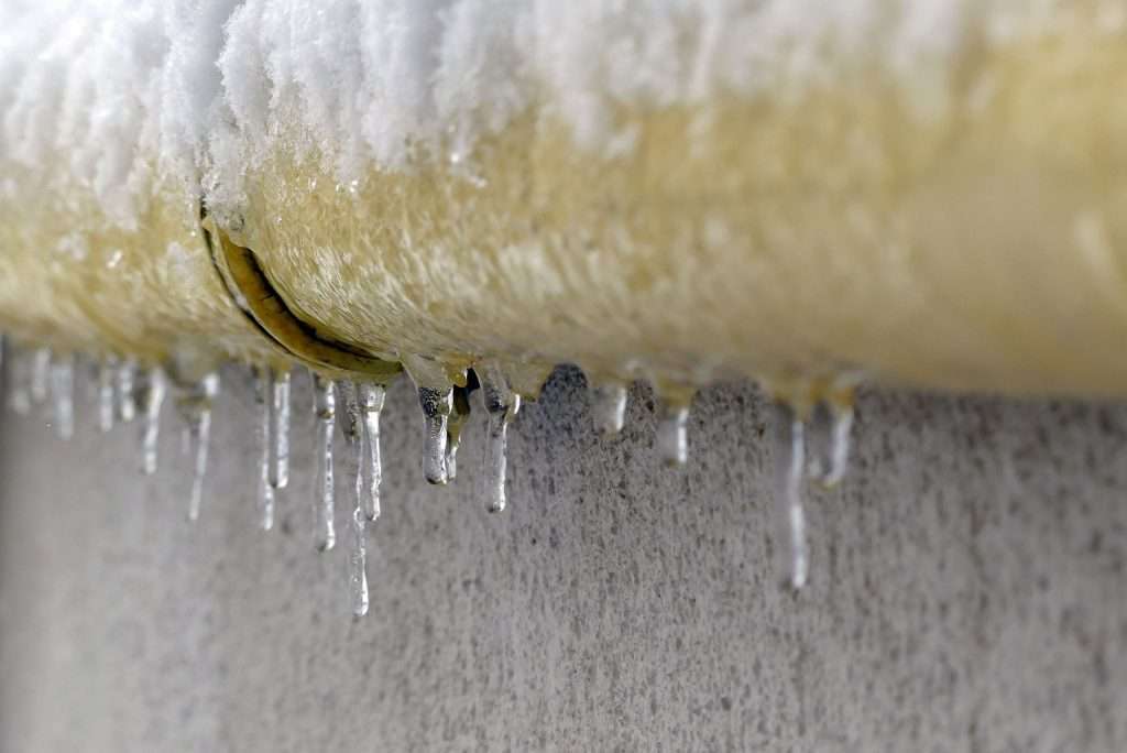 A yellow pipe on a cement wall, covered in ice and ice sickles